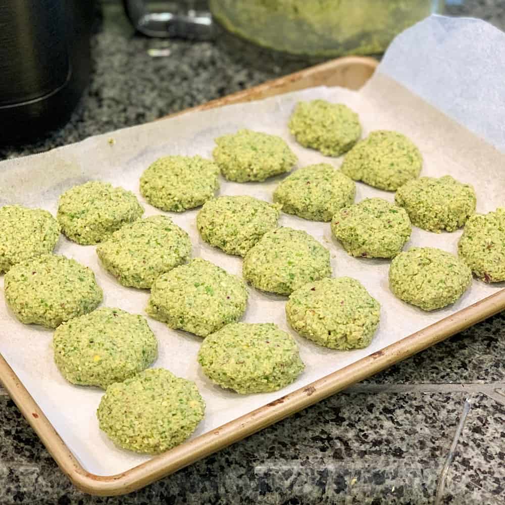 Falafel patties lined up on a parchment lined baking sheet for oven baking.