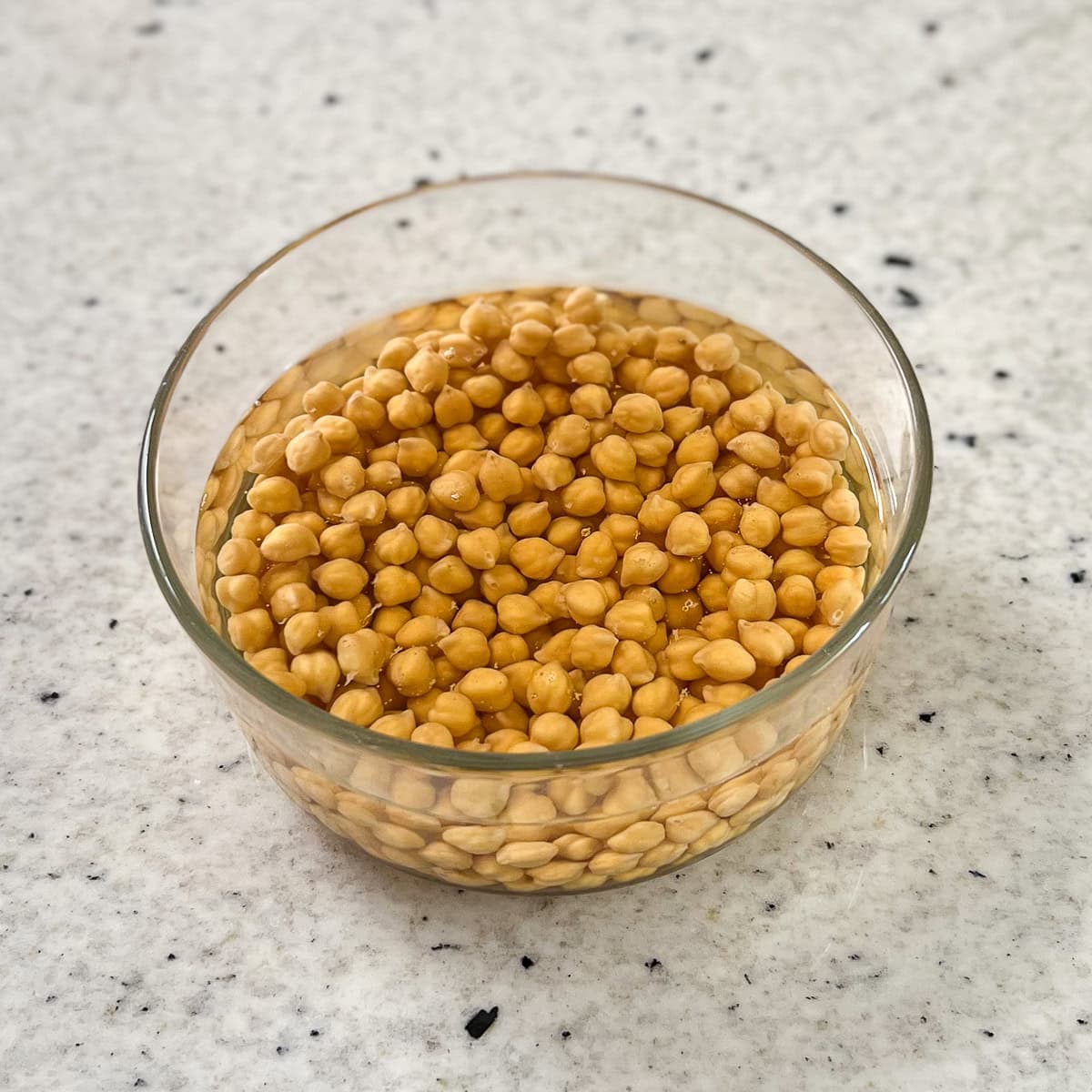 Chickpeas soaking in water in a glass bowl.