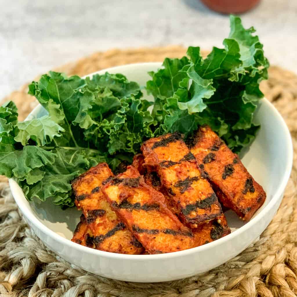 top side view of bbq tempeh slices in a white bowl with kale garnish