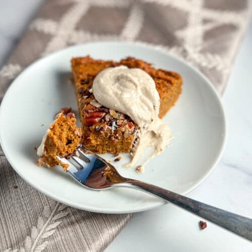side view close up of a slice of crustless sweet potato pie with a dollop of sweet cashew cream and fork with a bite