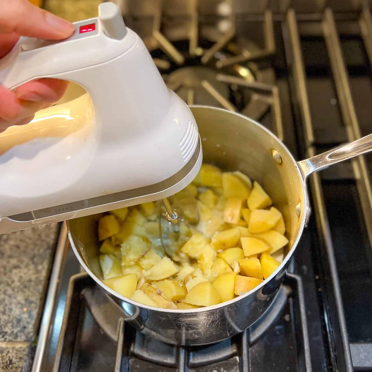 A hand mixer beating the cooked potatoes and garlic with soy milk.