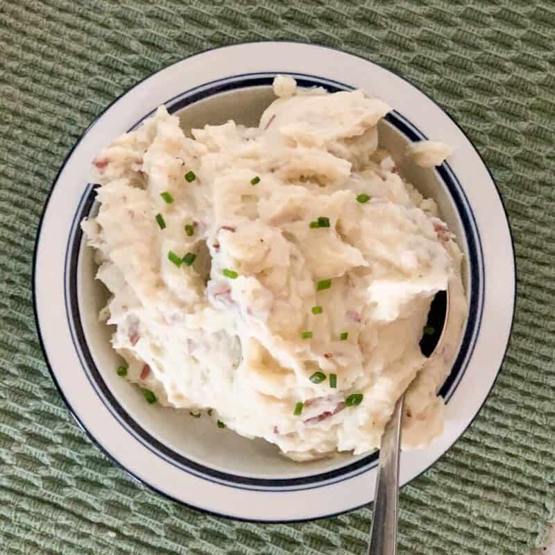 top view close up of steakhouse style garlic mashed potatoes in a white and blue rimmed bowl sitting on a woven green placemat