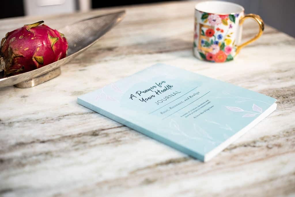 A Prayer for Your Health Journal book sitting on a granite countertop with colorful mug in background