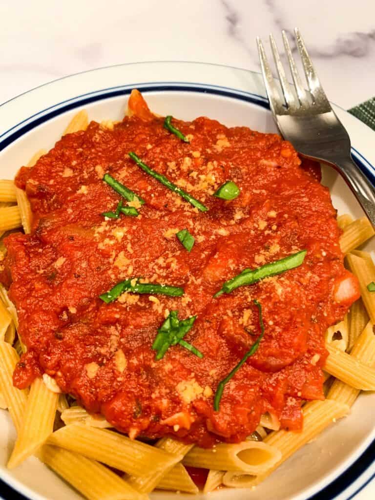 top view, close up of super simple 5-ingredient pasta marinara in a white bowl with a dark blue rim and fork balanced on the bowl. 