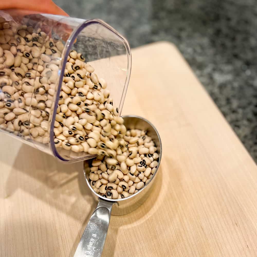 black eyed peas being poured into a measuring cup while sitting on a wooden cutting board