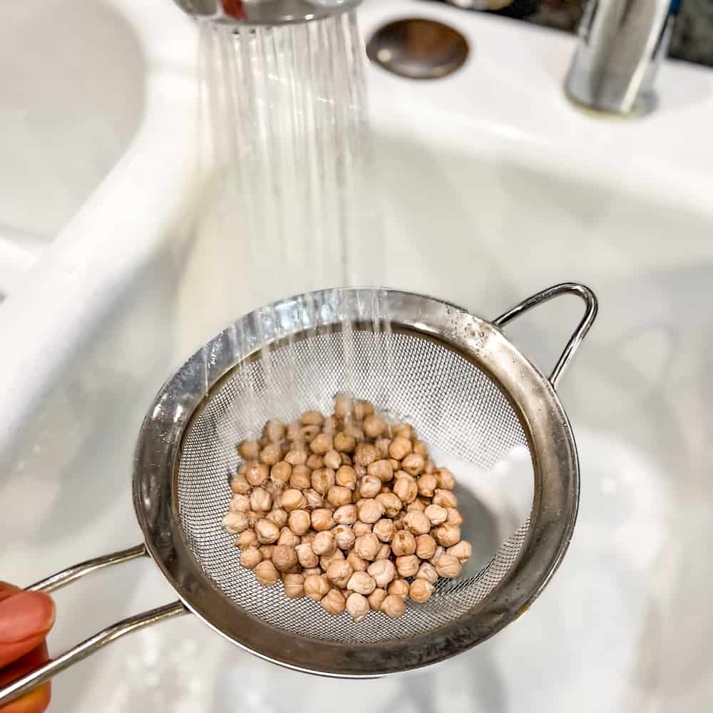 dried chickpeas being rinsed in a strainer over the sink