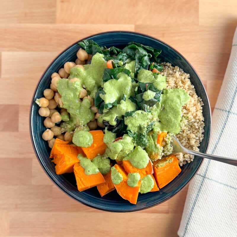 top view of buddha bowl with chickpeas, rainbow chard, quinoa, sweet potato, and green goddess sauce on top