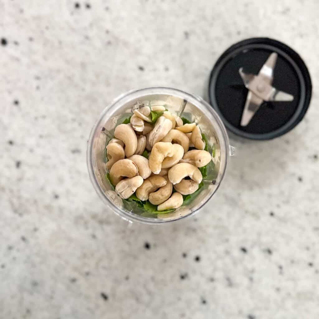Softened cashews in a mini blender cup with other ingredients.