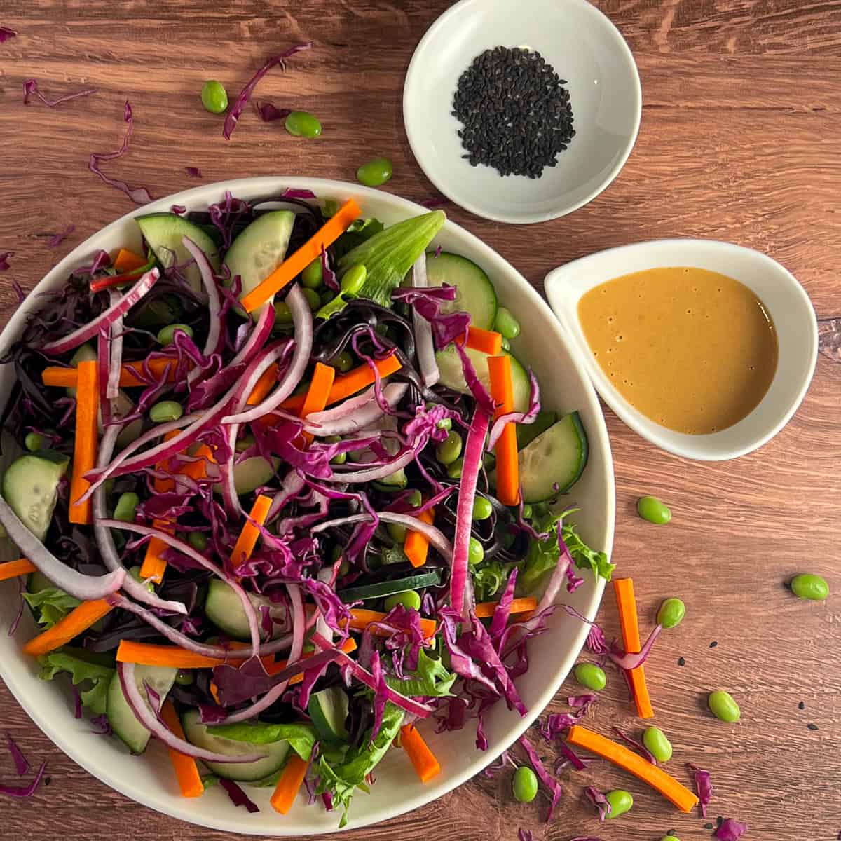 A bowl of Asian noodle salad with peanut sauce and black sesame seeds on the side. 