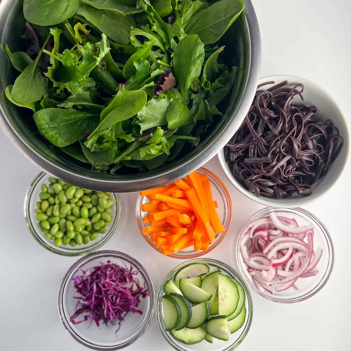 Ingredients for the Asian noodle salad: salad greens, black rice noodles, edamame, carrots, cucumbers, purple cabbage and red onion.