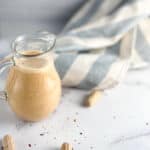 Peanut sauce in a small pitcher with loose peanuts scattered.
