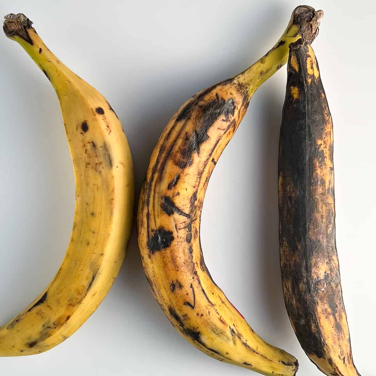 top view of three plantains of varying degrees of ripeness against a white surface