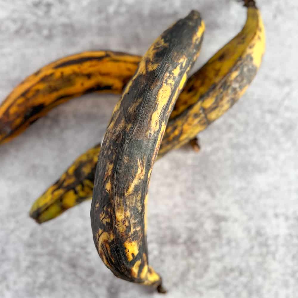 top view close up of three ripe plantains stacked on top of each other against a gray background