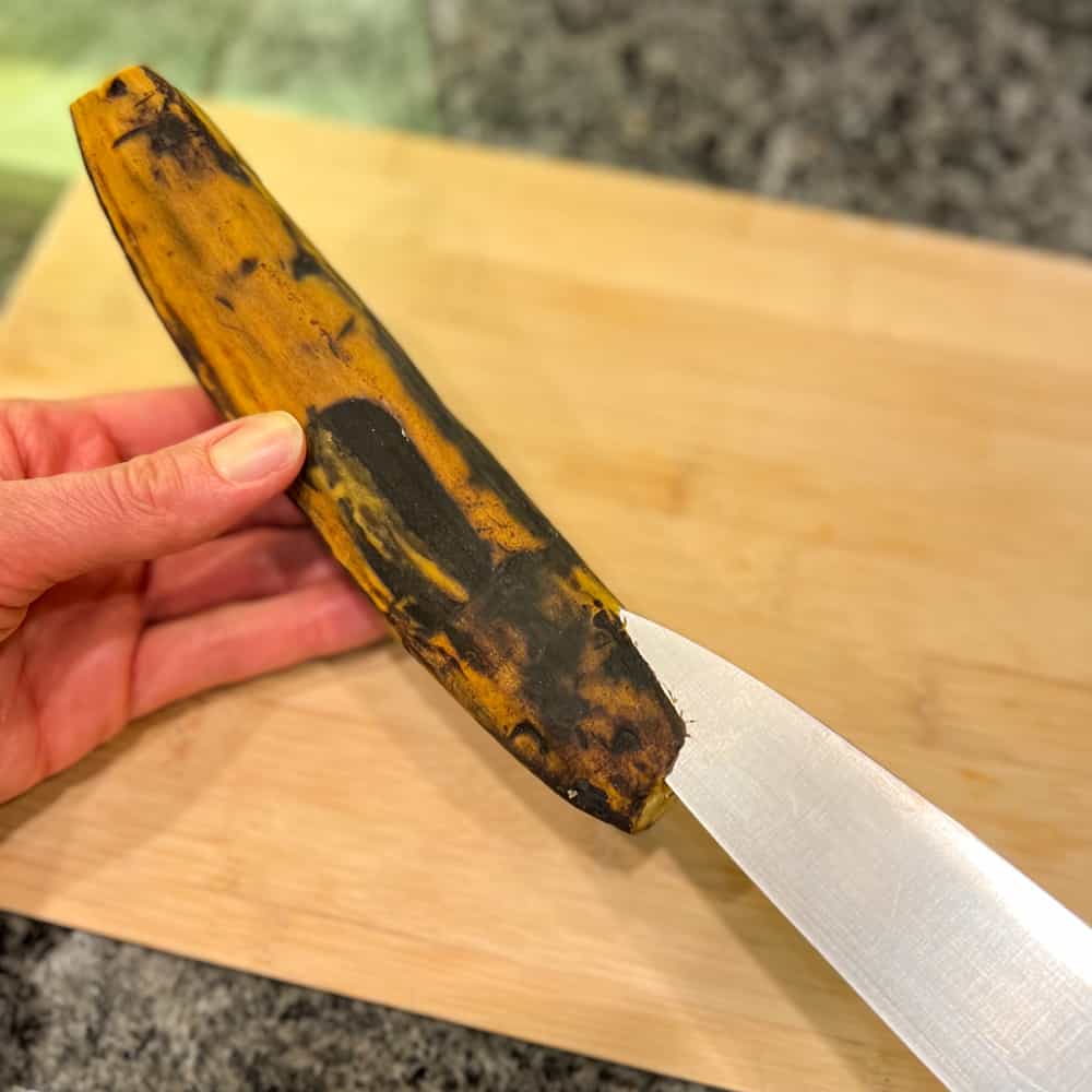 a ripe plantain being held in one hand and a knife in the other cutting a slit for peeling