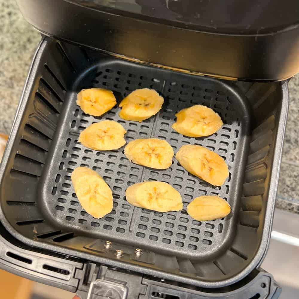 the ripe uncooked plantain slices that have been arranged in an air fryer basket