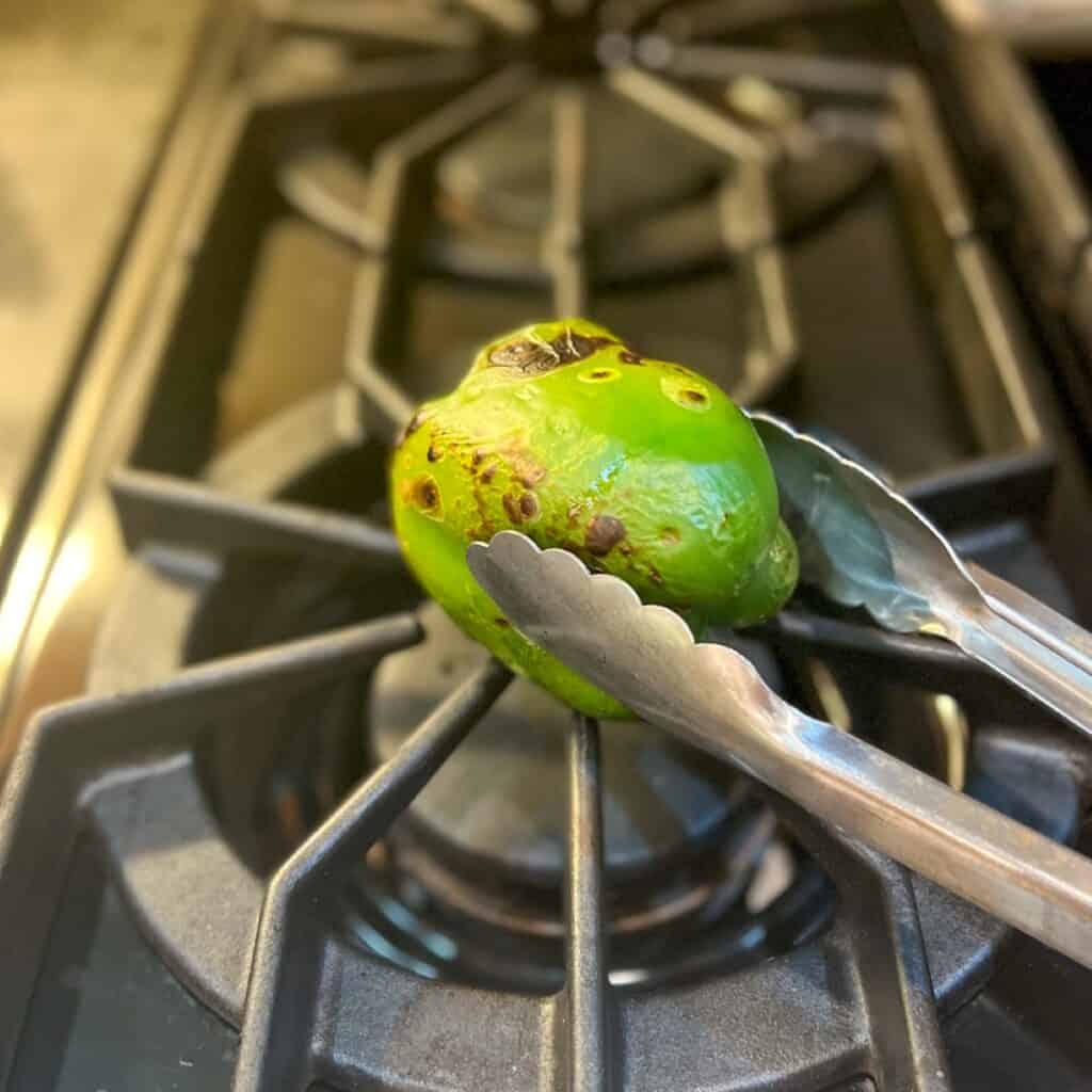 A green bell pepper being charred on the stovetop.