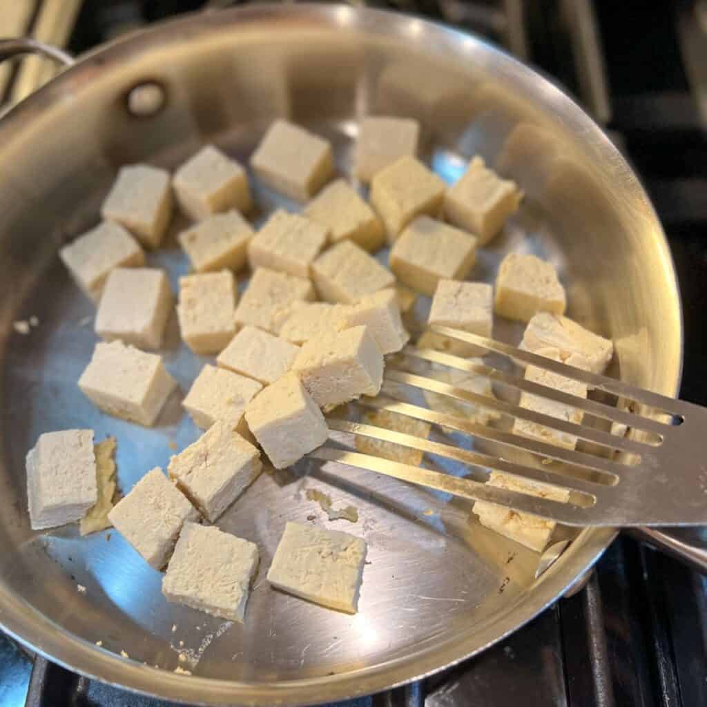 Tofu chunks being cooked in the skillet.
