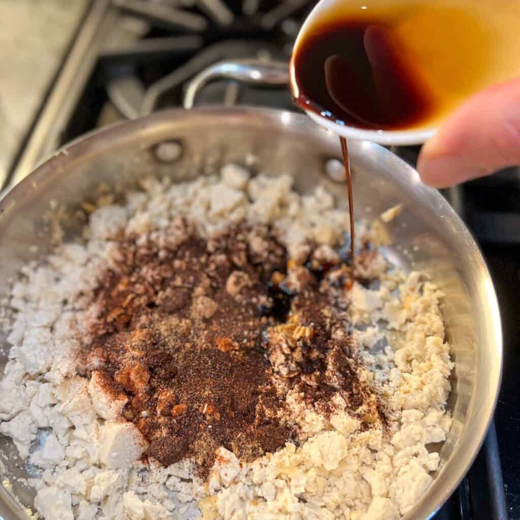 Seasonings being added to the skillet with tofu.