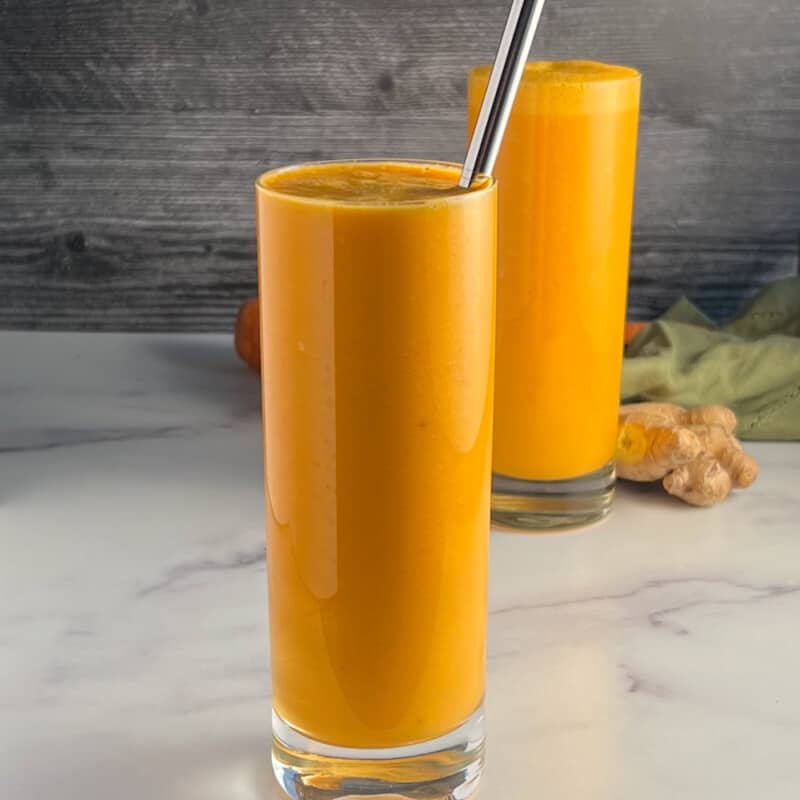 Side view of two glasses of spicy orange creamsicle smoothie with ginger and green towel blurred in the background