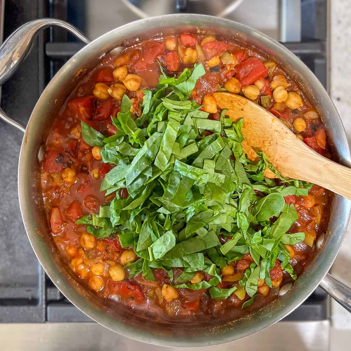 Chopped spinach being added to the vegan chana masala.