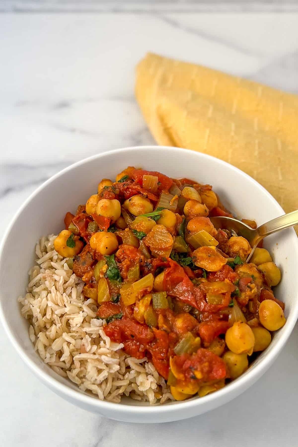Vegan chana masala in a bowl with a side of brown rice.