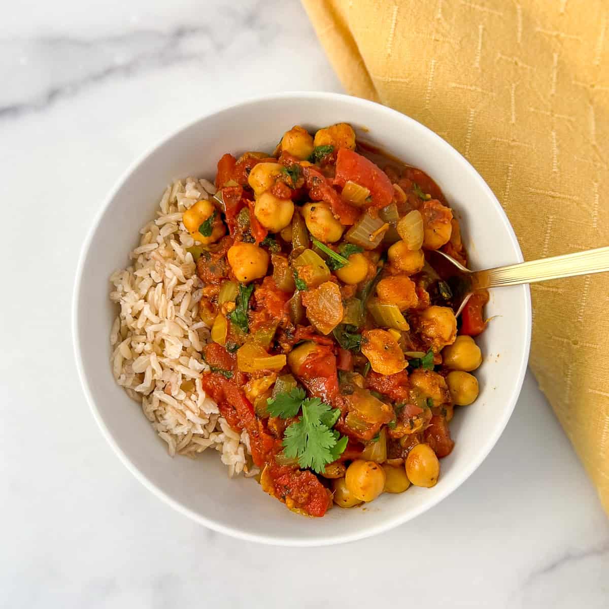 Vegan chana masala in a bowl with a side of brown rice.