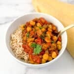 A bowl of vegan chana masala with a side of brown rice.