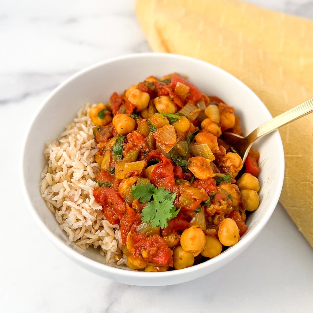 A bowl of vegan chana masala with a side of brown rice.