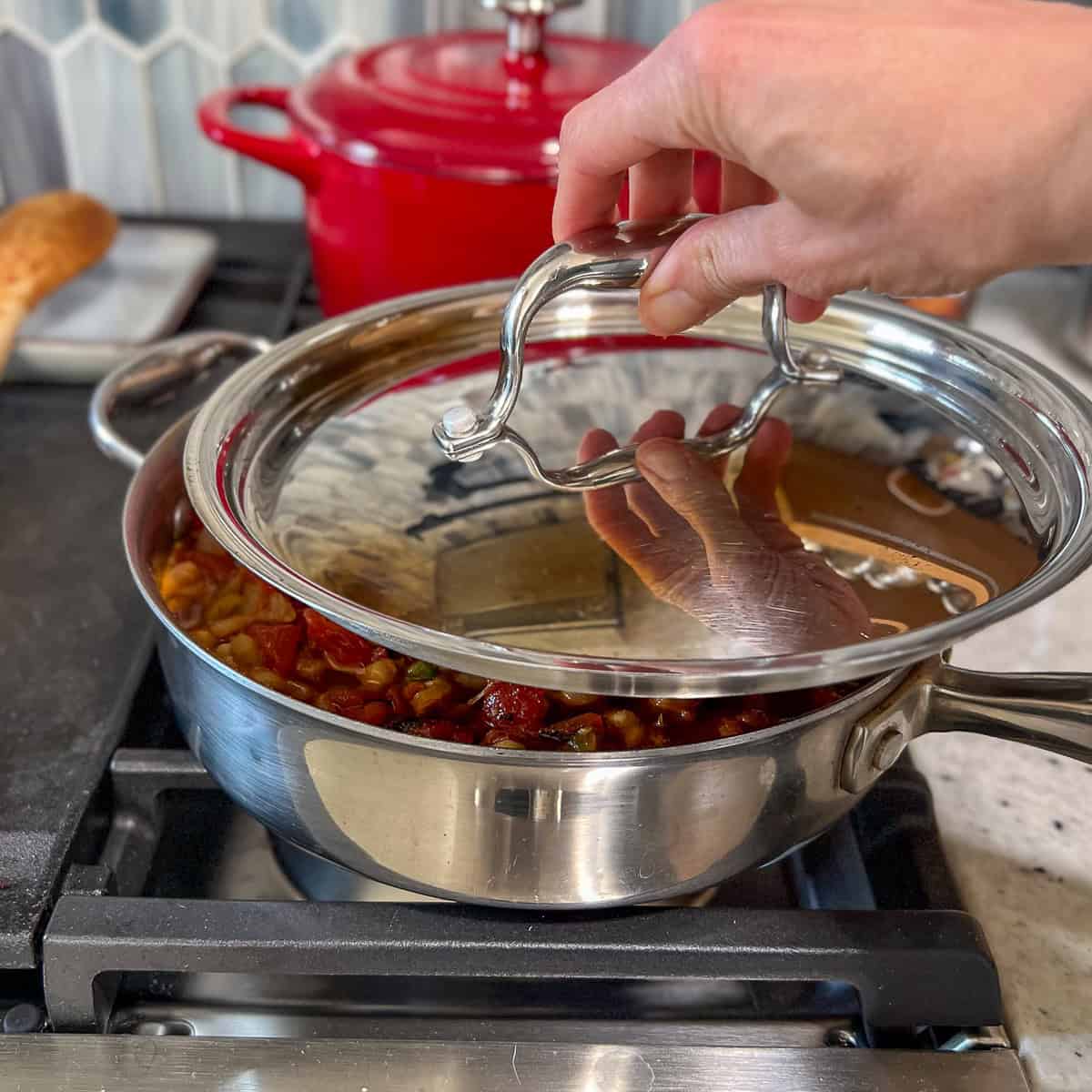 A woman's hand putting a lid on a sauté pan, partially covered.