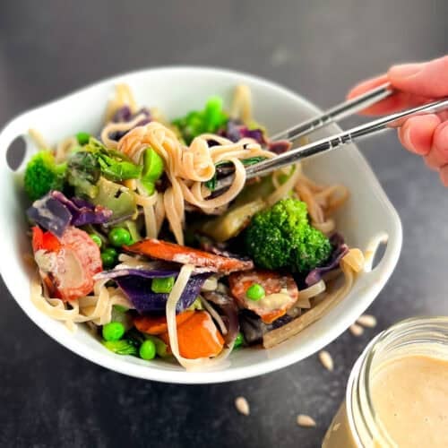 A woman's hand using chopsticks to pick up veggie stir fry with noodles.