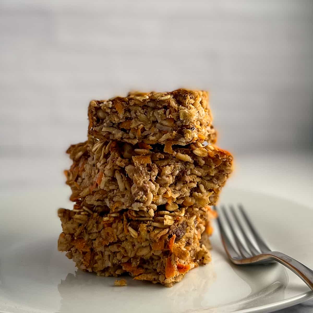 side view close up of 3 squares of carrot cake baked oatmeal on a white plate and fork on the side