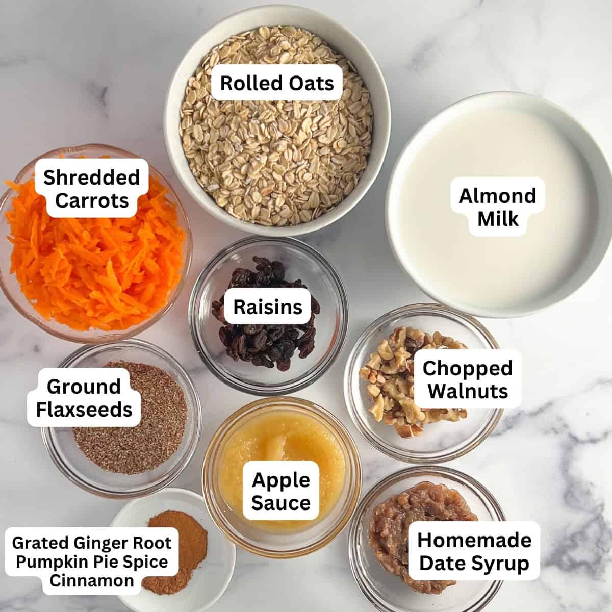 Ingredients for carrot cake baked oatmeal: rolled oats, almond milk, shredded carrots, raisins, chopped walnuts, applesauce, homemade date syrup, ground flaxseeds and spices.