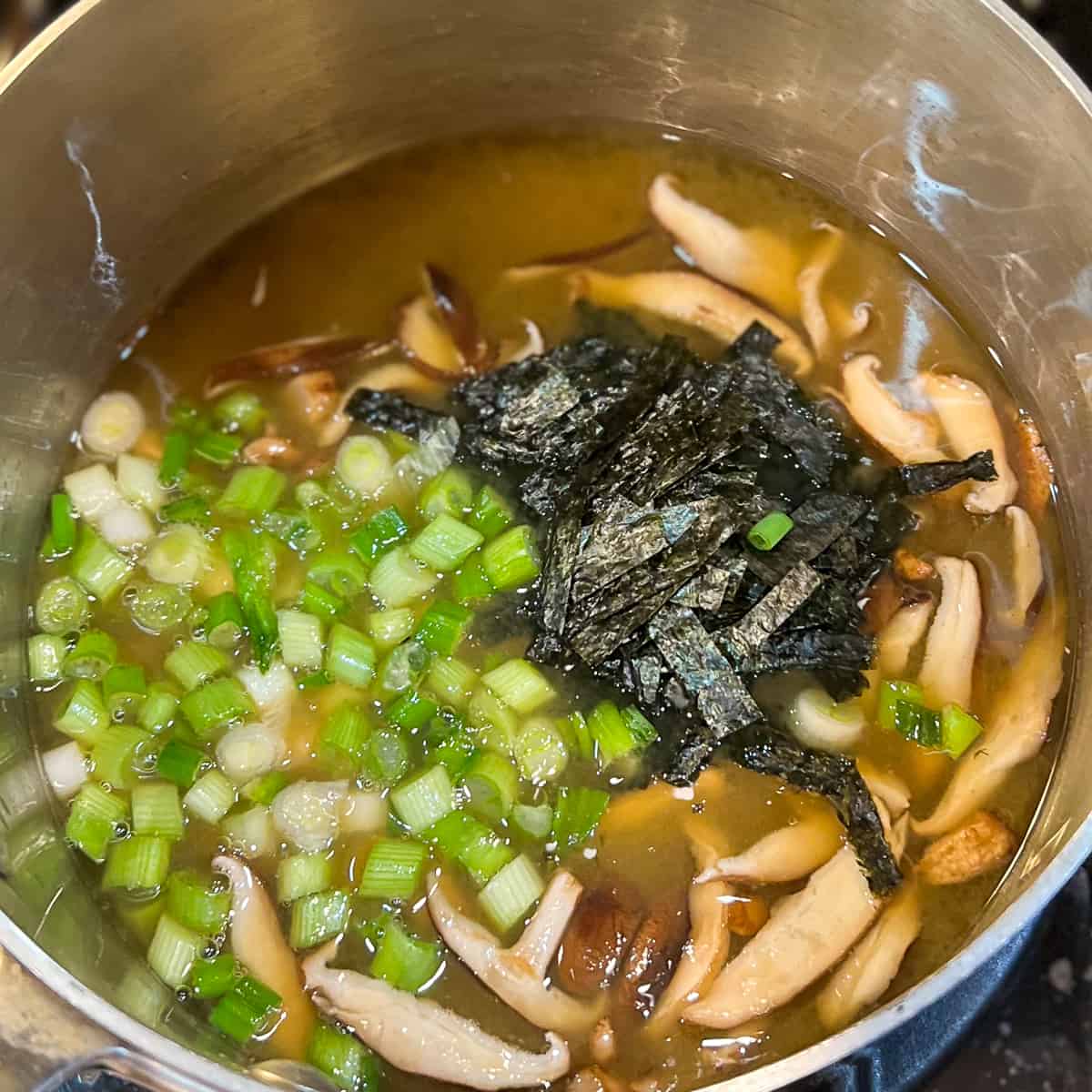 top view of pot on a stove with vegetable broth, tofu, green onion and nori seaweed