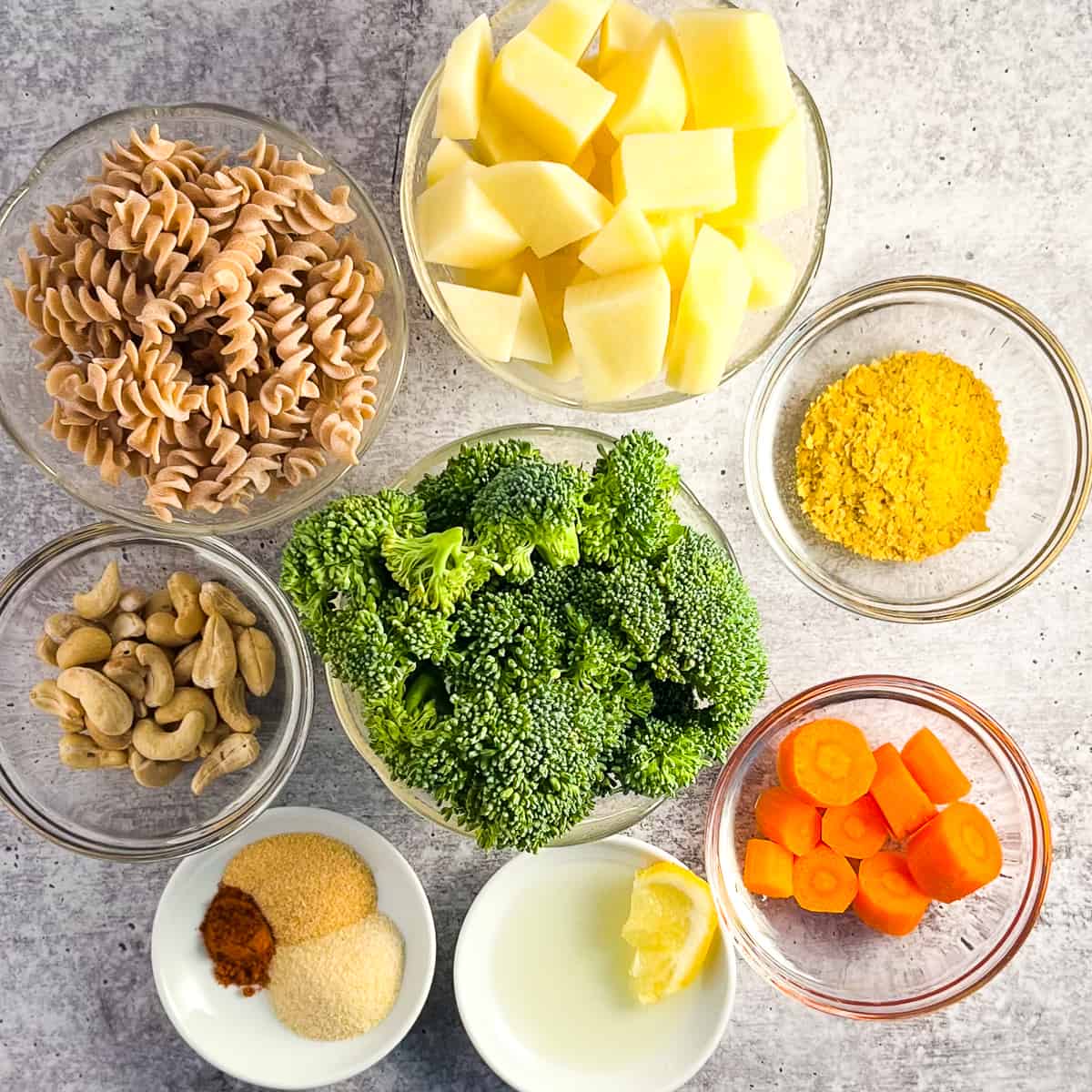 Top view of the ingredients for vegan mac and cheese. potato, nutritional yeast, carrots, broccoli, lemon juice, whole wheat pasta, cashews, garlic powder, onion powder and cayenne pepper