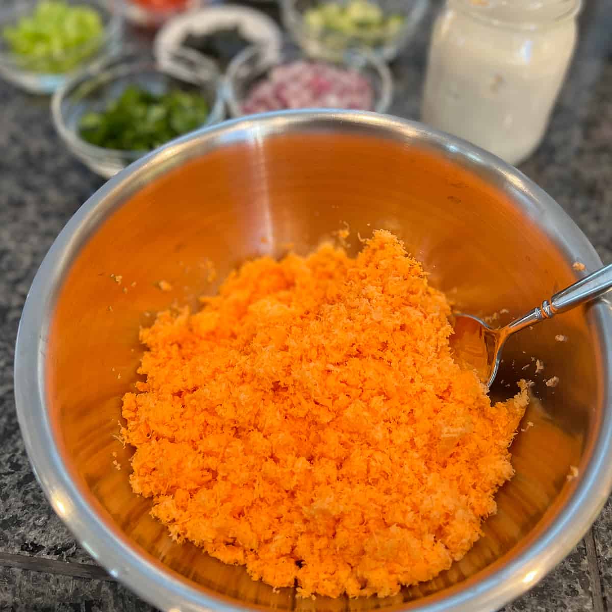 shredded carrots for vegan tuna salad in a stainless steel bowl with other ingredients blurred in the background