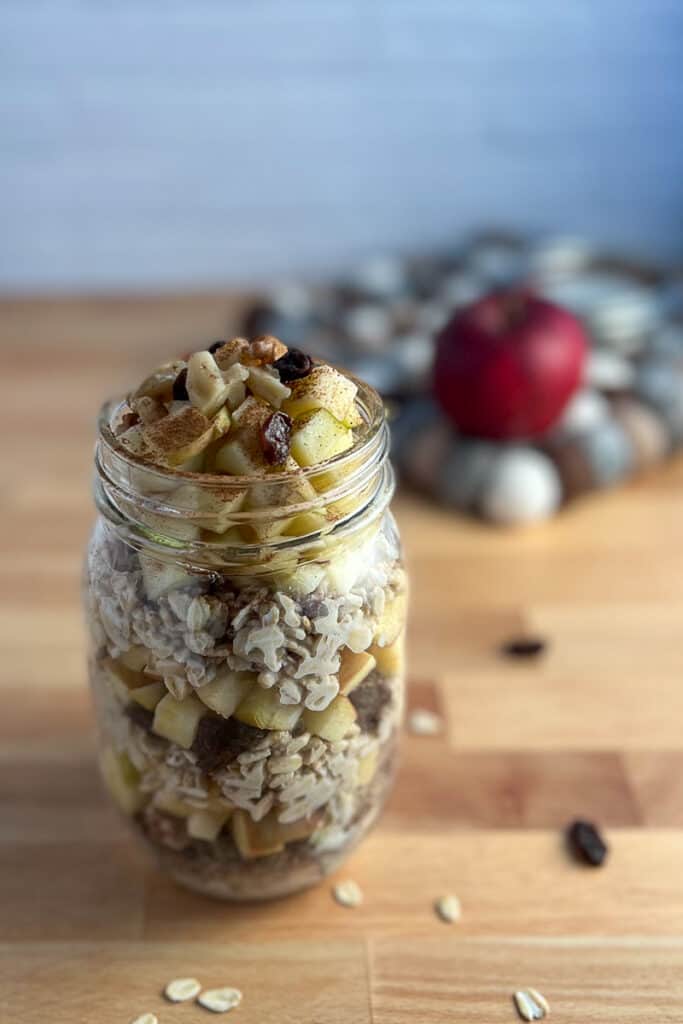 side view close up of apple cinnamon overnight oats in a mason jar sitting on a wooden surface, with apple blurred in the background