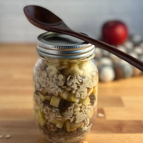 Side view of a mason jar with apple cinnamon overnight oats and a wooden spoon balanced on top.