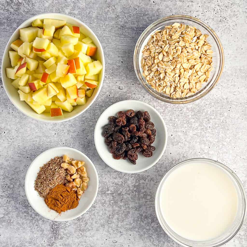 top view of ingredients for apple cinnamon overnight oats: diced apple, rolled oats, unsweetened almond milk, raisins, ground flaxseeds, chopped walnuts, cinnamon