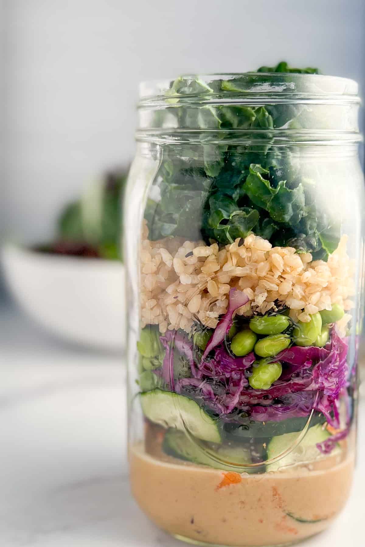 side view close up of Asian salad in a jar with a bowl of mixed salad greens blurred in the background.