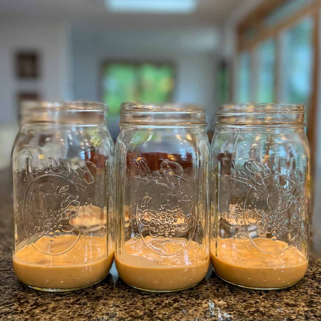 three 32 ounce glass mason jars lined up on a kitchen counter with ⅓ cup peanut sauce at the bottom
