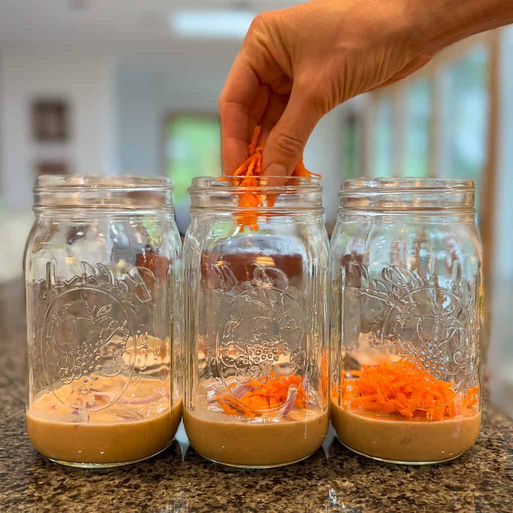 three mason jars with shredded carrot being added