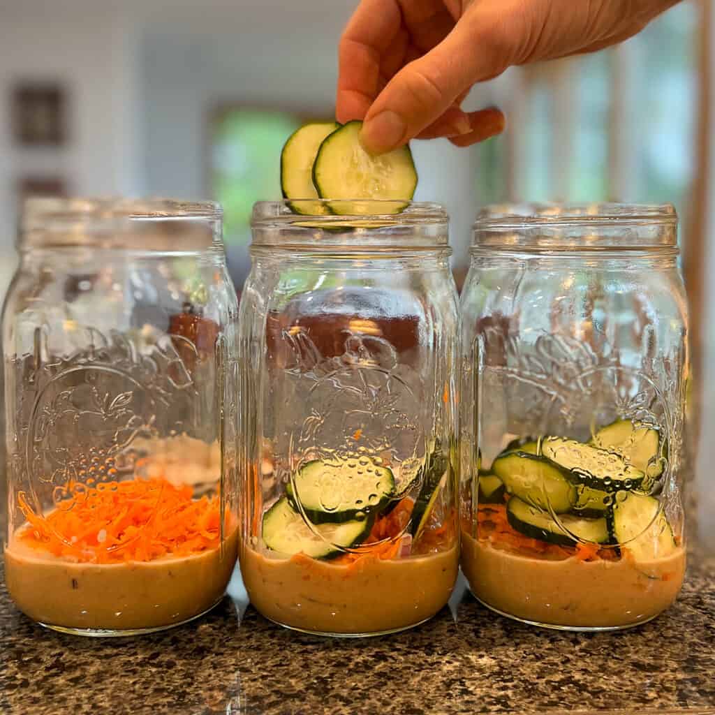 three mason jars with sliced cucumbers being added