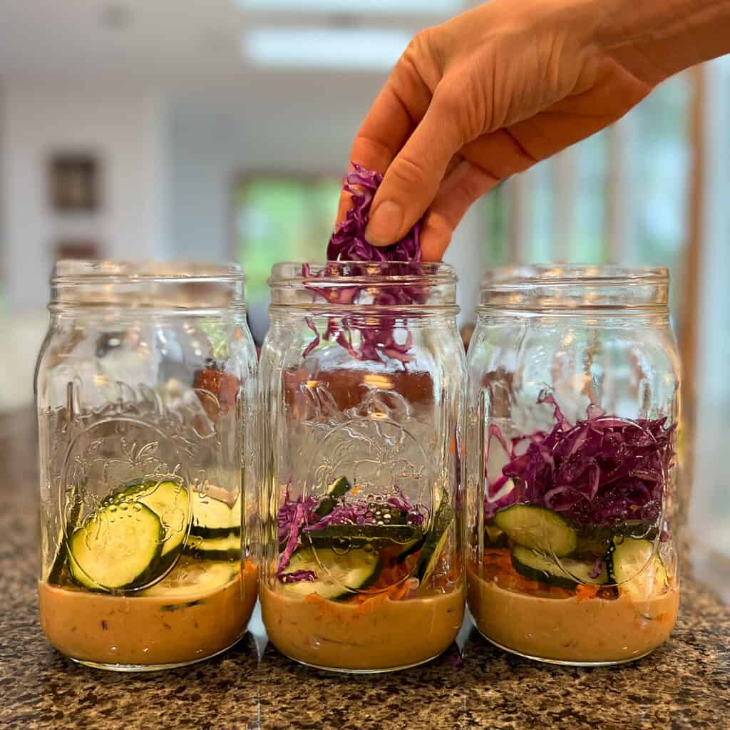 three mason jars with thinly sliced purple cabbage being added