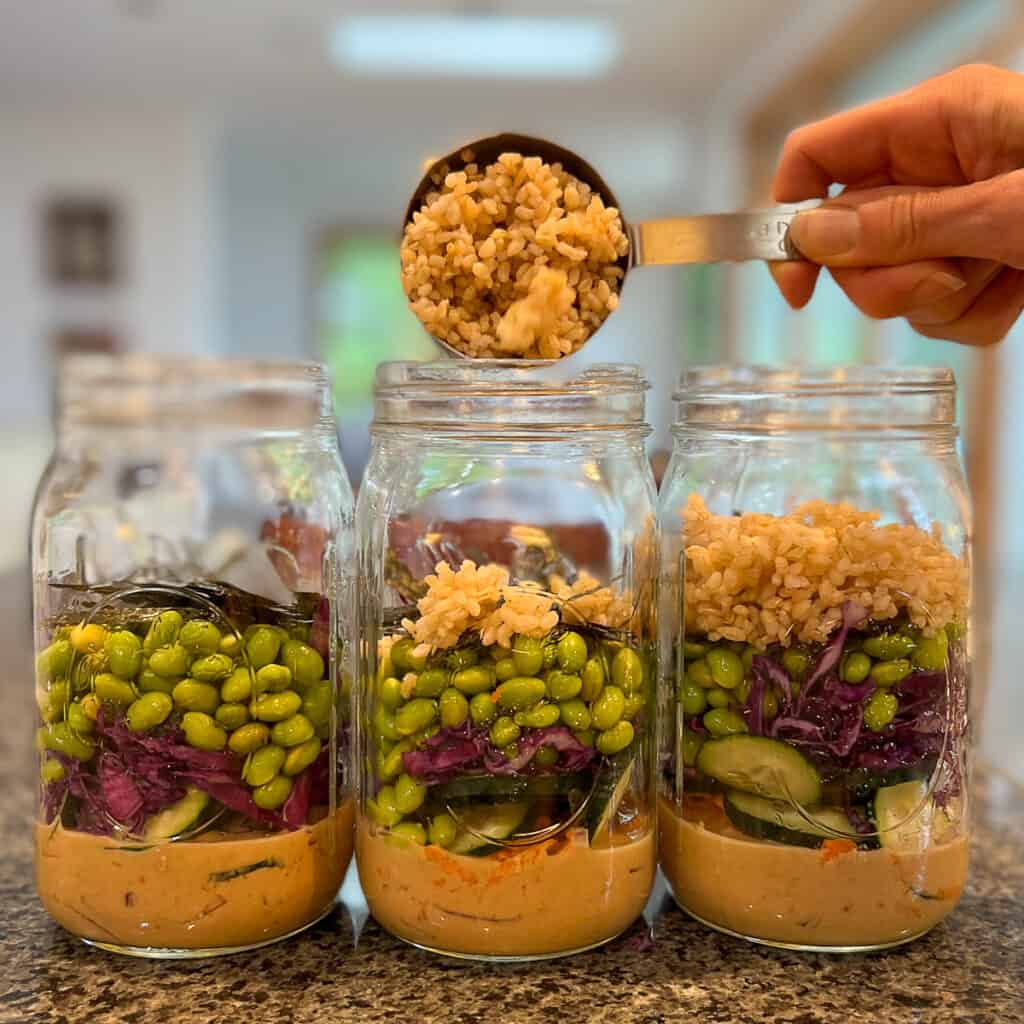three mason jars with ½ cup cooked brown rice being added to each jar