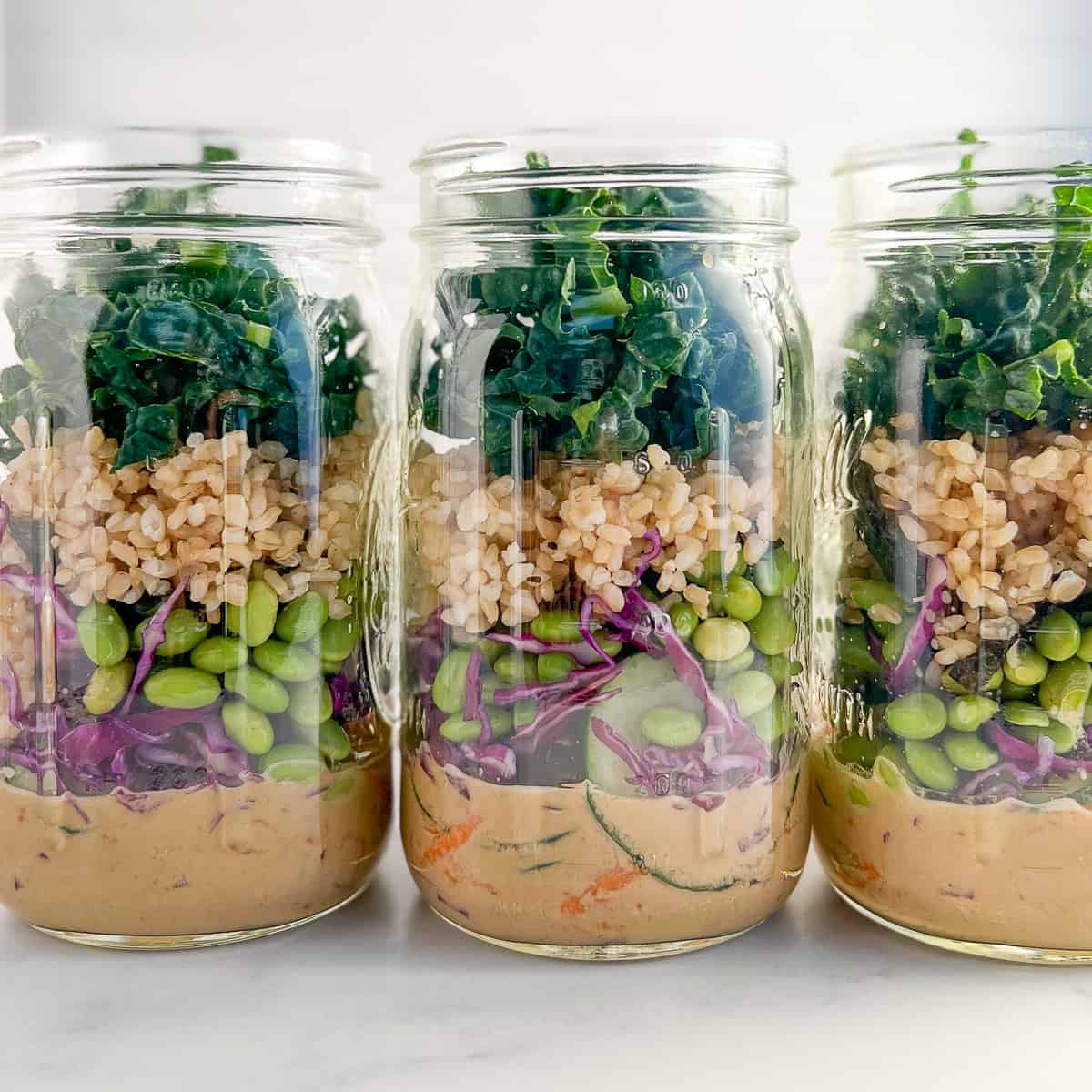side view close up of 3 Asian salads in a jar lined up on a white marble surface