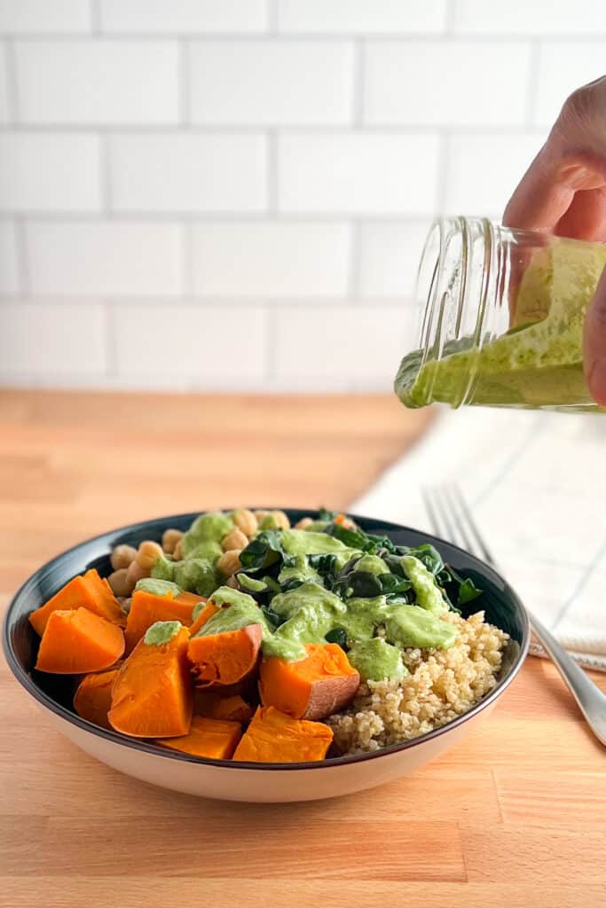 side view of fast and easy buddha bowl with green goddess dressing being poured on it