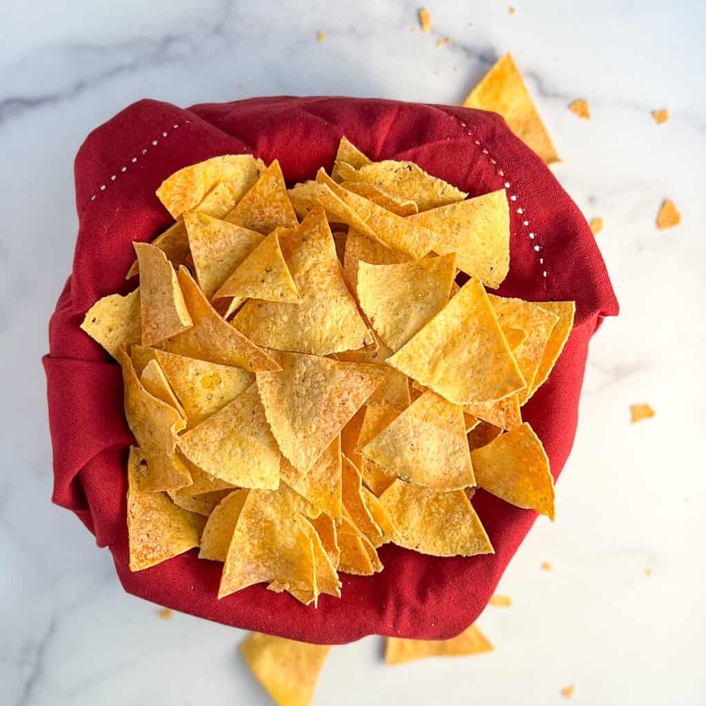 top view of oven baked tortilla chips in a bowl lined with a red napkin on a marble surface