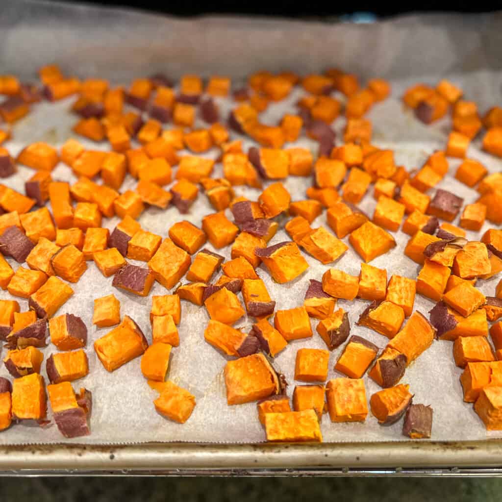Diced cooked sweet potatoes on a parchment lined baking sheet coming out of the oven
