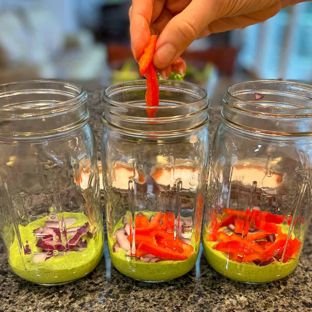 3 mason jars lined up with chopped red bell pepper being added