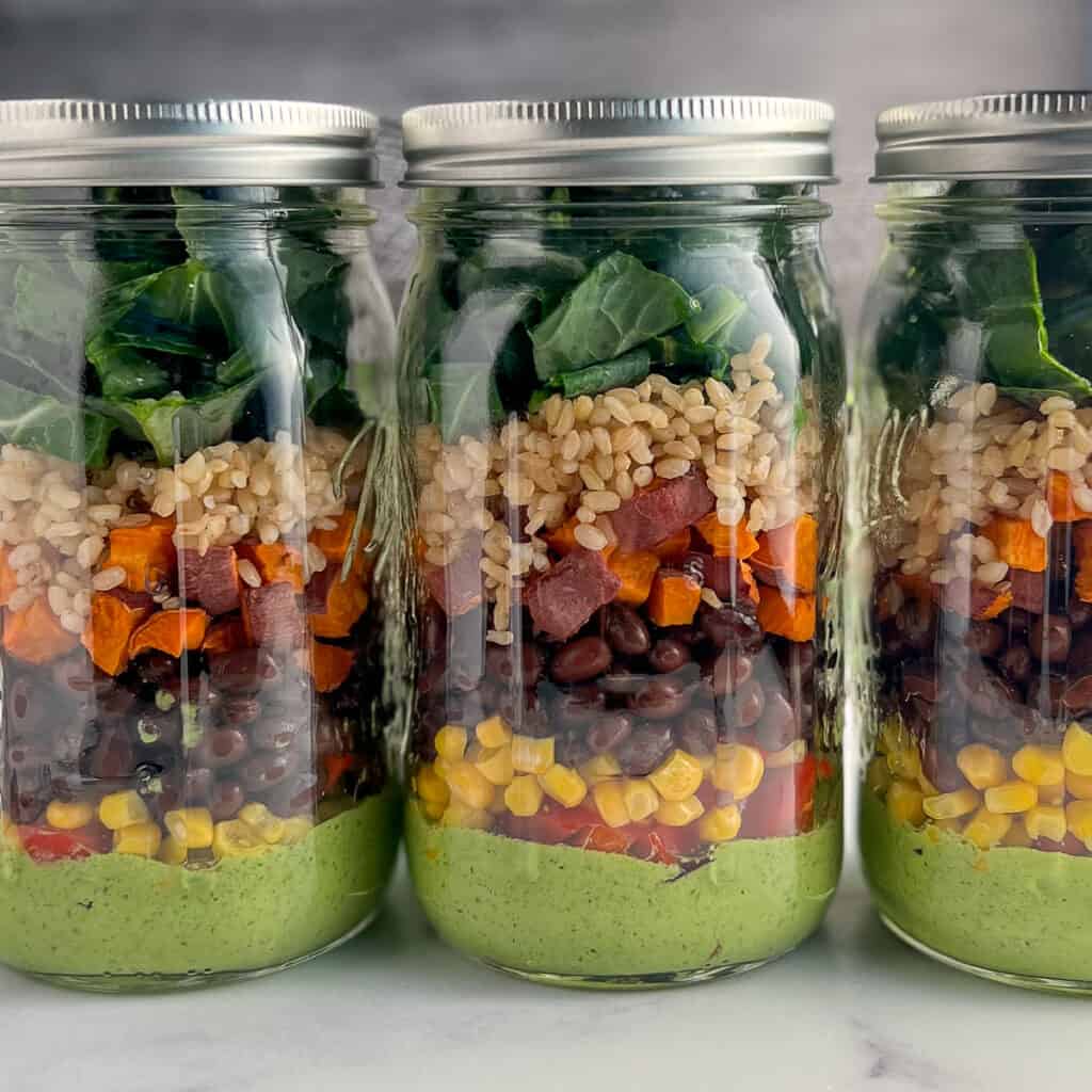 three mason jars with southwestern salads - green goddess dressing, peppers, corn, black beans, sweet potato, rice collard greens